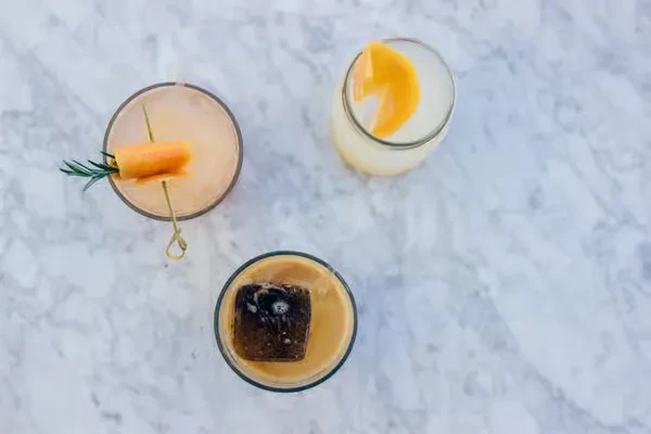 Three different cocktails, garnished with carrot, citrus peel, and coffee ice.