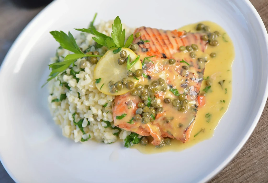 Golden-brown grilled salmon with caper sauce, rice, lemon, and parsley.