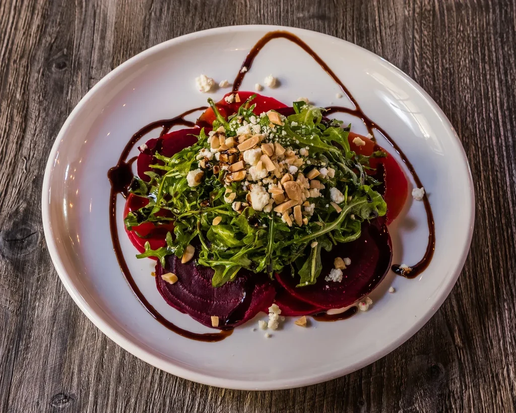 Beet and arugula salad with cheese, almonds, balsamic, on wood table.