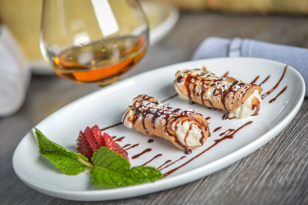 Two cannoli drizzled with chocolate, garnished with strawberries and mint.