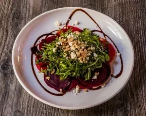 Plated beet and arugula salad with cheese, nuts, balsamic glaze.