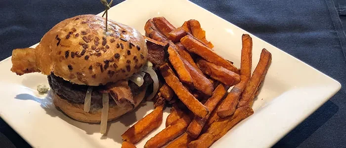 Gourmet burger with cheese, bacon, and sweet potato fries on a plate.