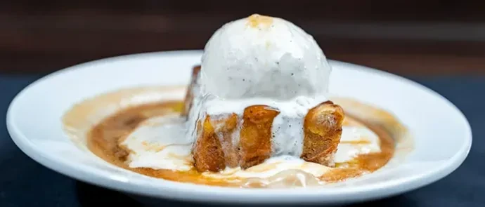 Golden-brown dessert with melting ice cream and syrup on white plate.