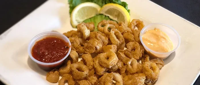Fried calamari with two sauces, lemon wedges, and lettuce on a white plate.