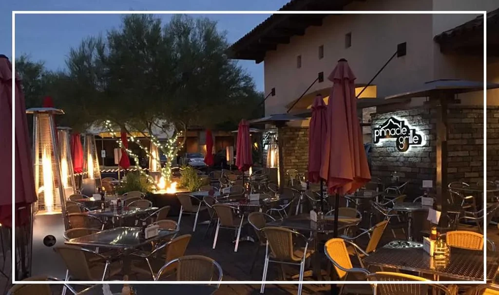 Empty 'Pinnacle Grille' patio with heaters, string lights, and folded umbrellas.