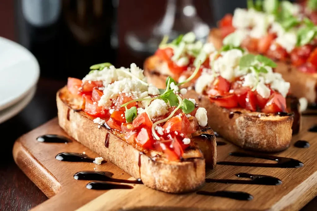 Three bruschetta with tomatoes, cheese, microgreens, balsamic glaze on a board.