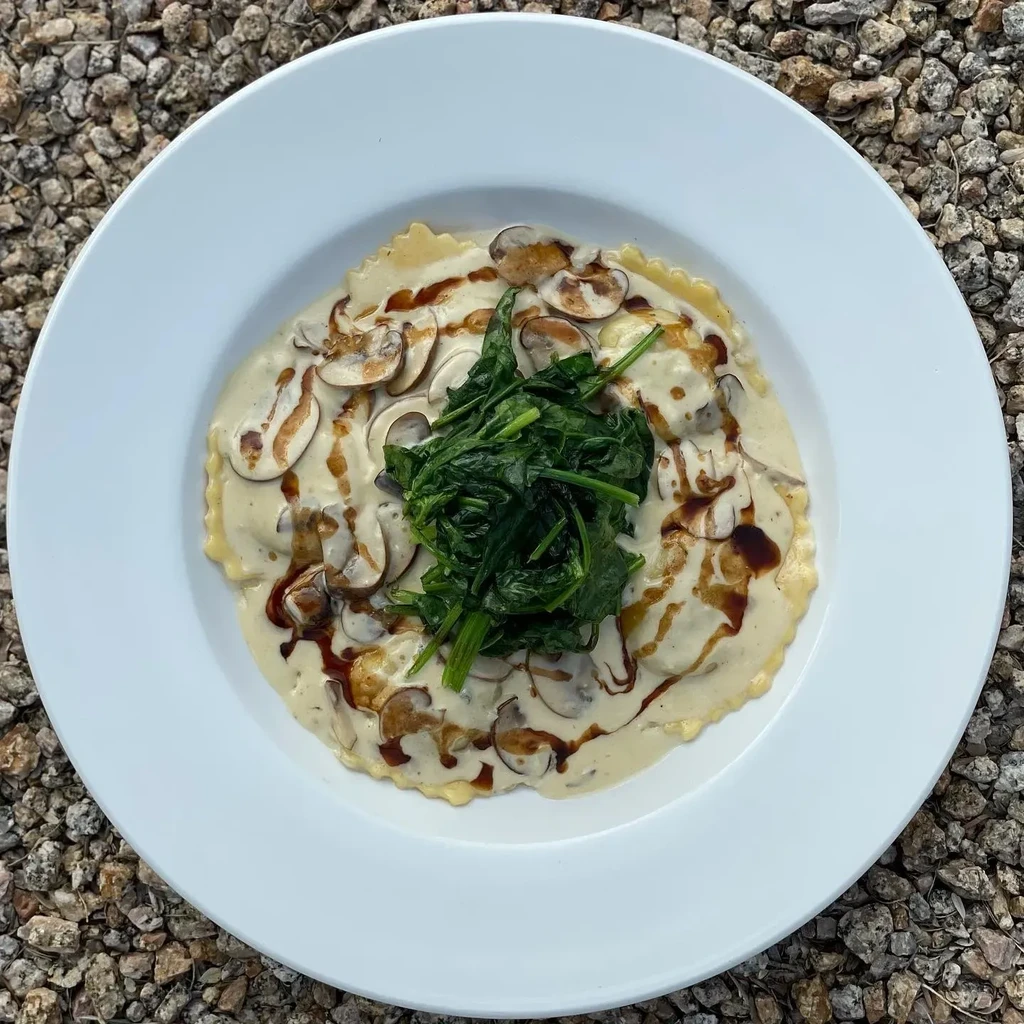 Plate of pasta with creamy sauce, mushrooms, spinach, and dark drizzle.