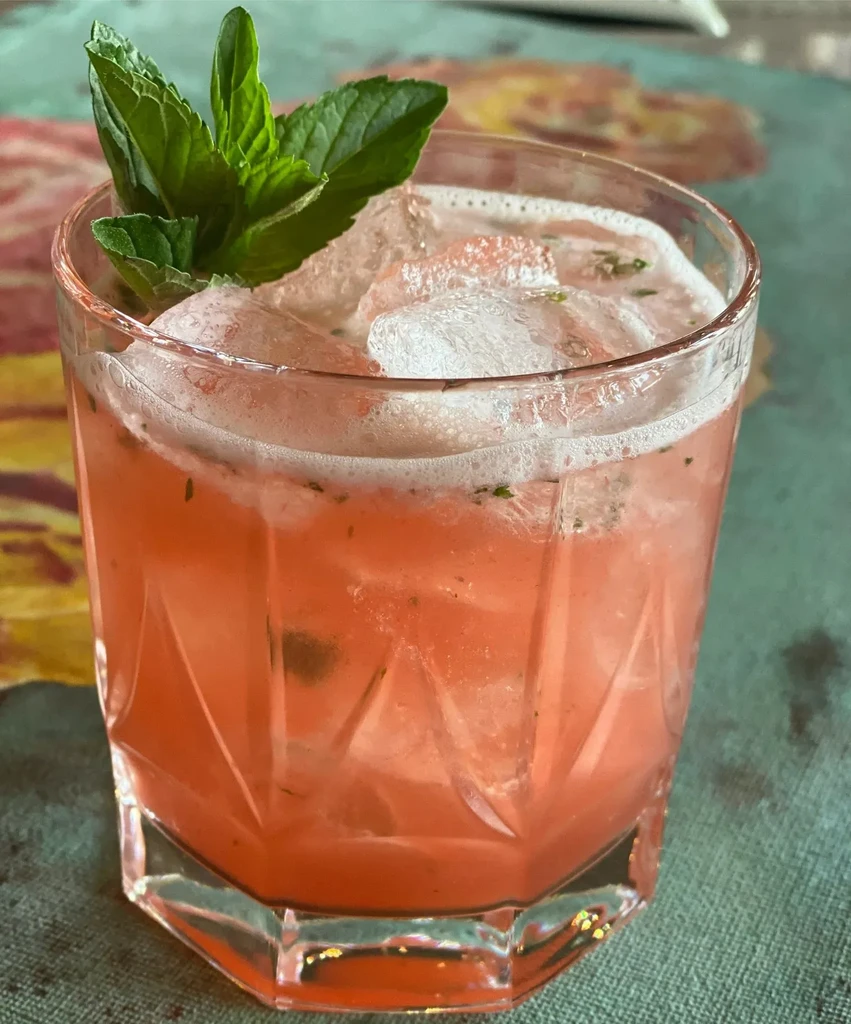 Close-up of pink cocktail with ice and mint in a faceted glass.