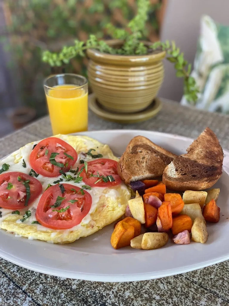 Breakfast plate: omelet with tomatoes, roasted potatoes, and toast.