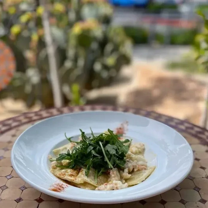 Pasta with creamy sauce and arugula on a mosaic outdoor table.