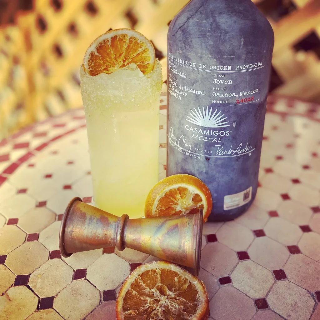 Still life with margarita-like cocktail, Casamigos Mezcal, jigger, and orange slices.