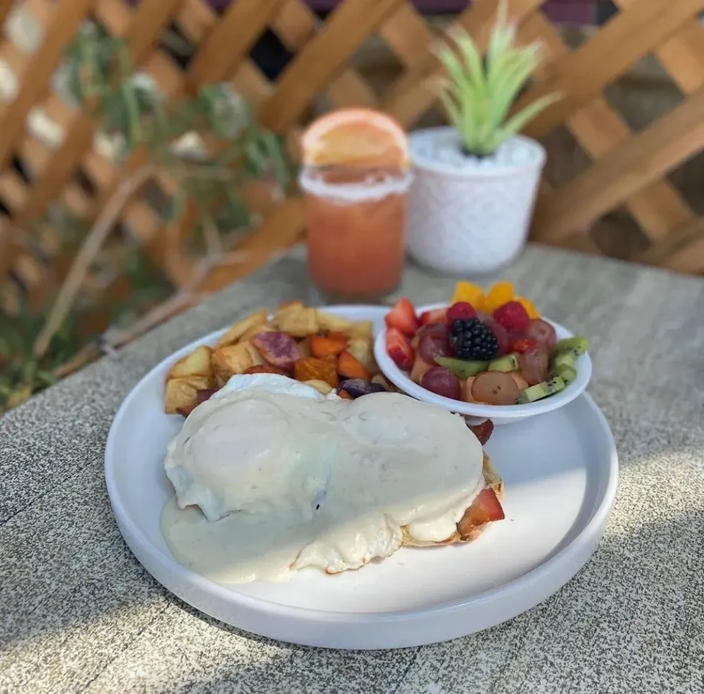 Eggs Benedict with roasted vegetables and fruit on a patio table.