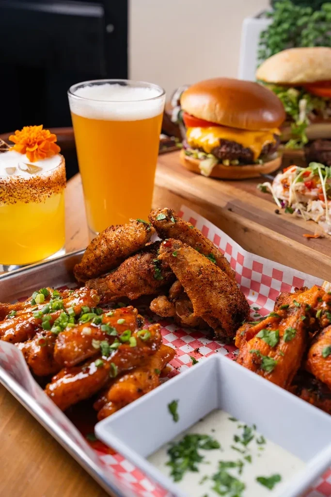 Multiple styles of chicken wings, burgers, beer, and a garnished cocktail.