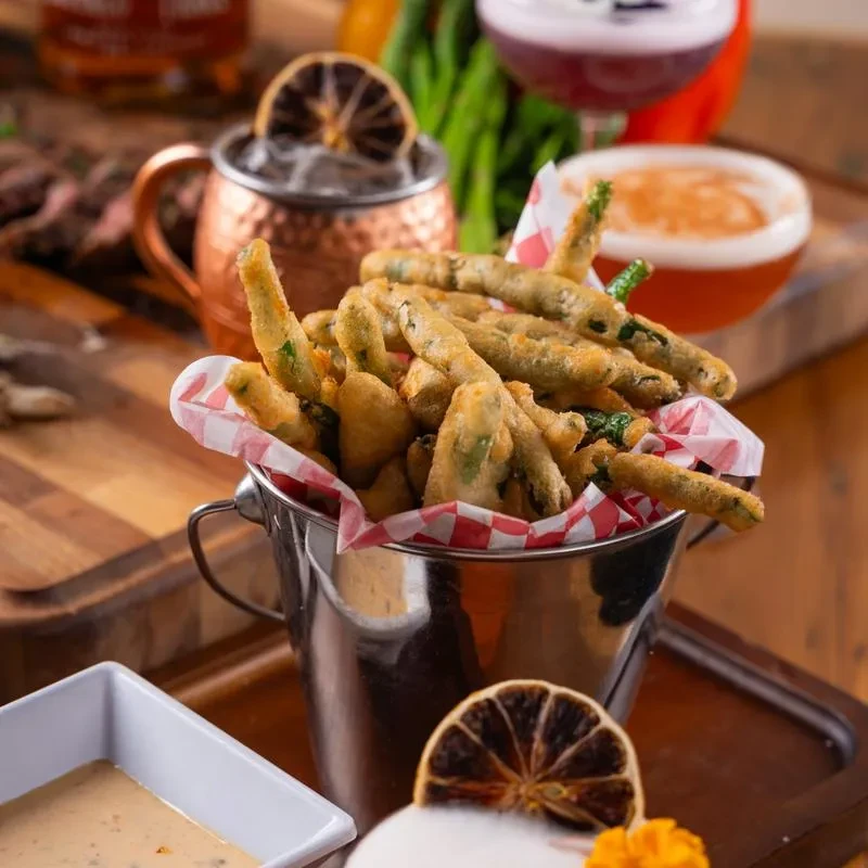 Bucket of fried green beans with dipping sauce in a restaurant setting.