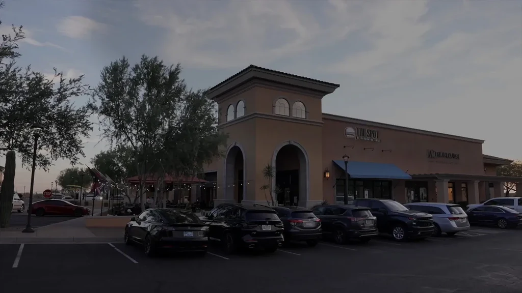 Dark, Mediterranean-style strip mall with businesses at dusk.