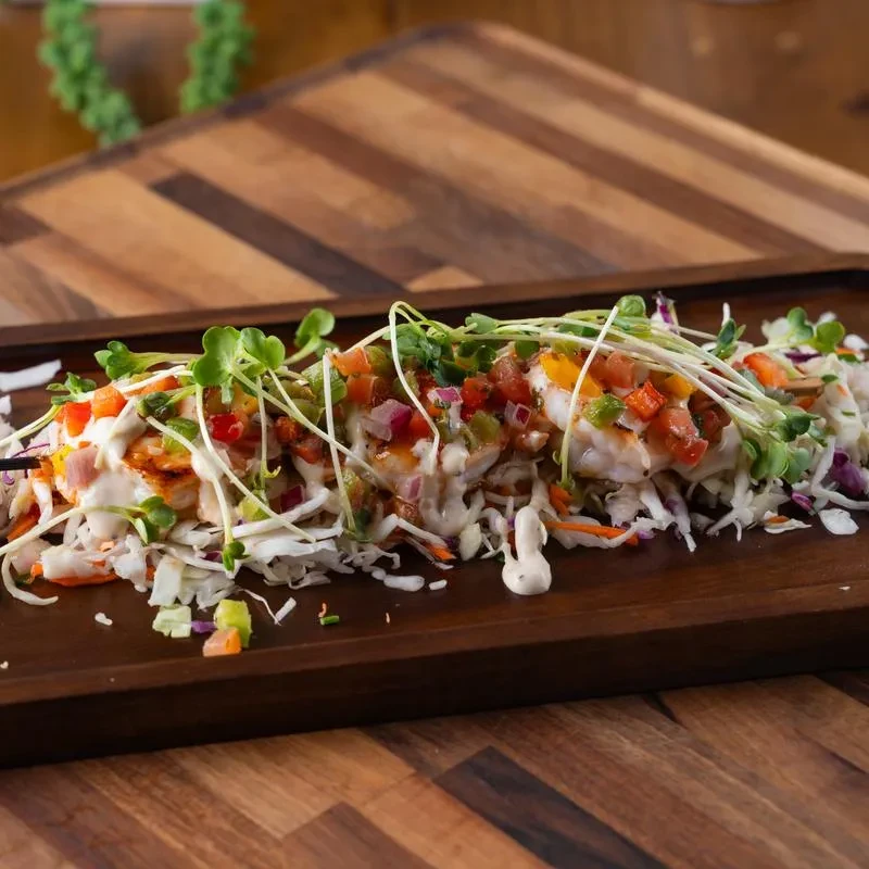 Grilled protein with salsa, sauce, cabbage, and microgreens on wood platter.