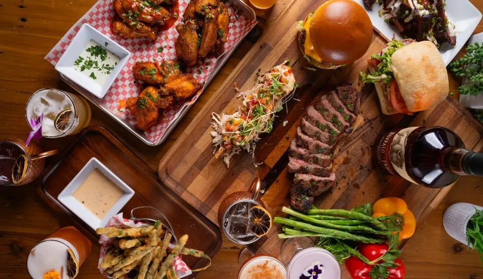Overhead flat-lay of chicken, steak, burger, cocktails, Buffalo Trace whiskey.