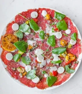 Thinly sliced beef carpaccio with cheese, greens, capers, and dried orange.