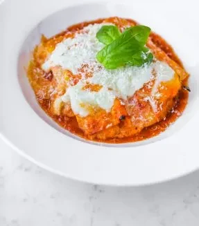 Baked pasta layers with tomato sauce, melted cheese, and basil.