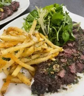 Steak frites with a side salad on a white plate.