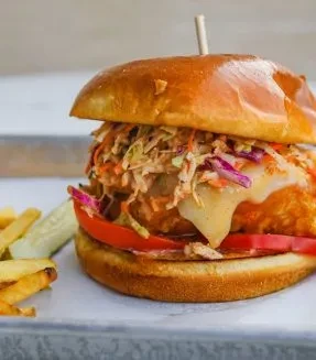 Close-up of a fried chicken or fish sandwich, coleslaw, fries, and pickle.