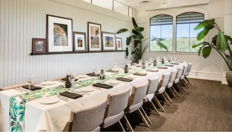 Bright dining room with tropical runner, botanical art, and potted plants.