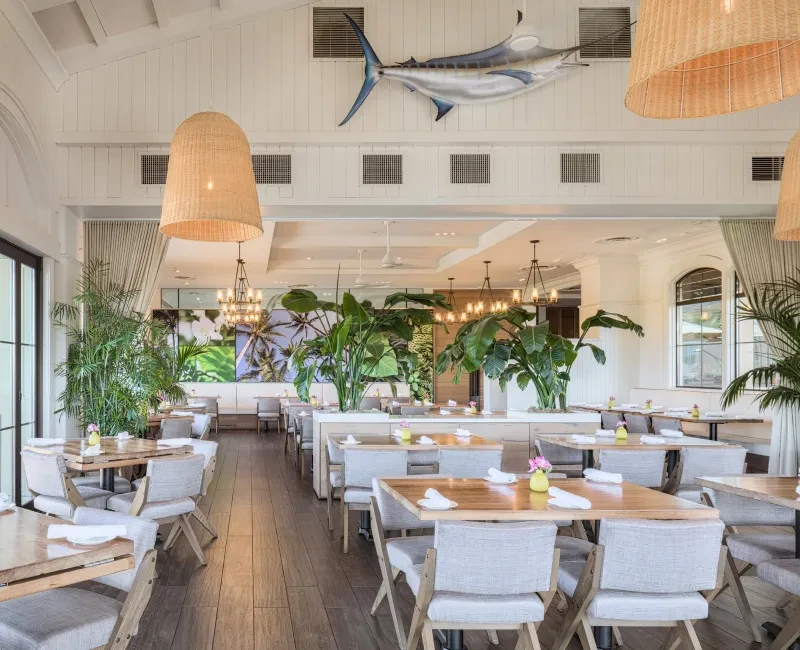Bright, airy restaurant with tropical plants, wicker lights, and marlin sculpture.