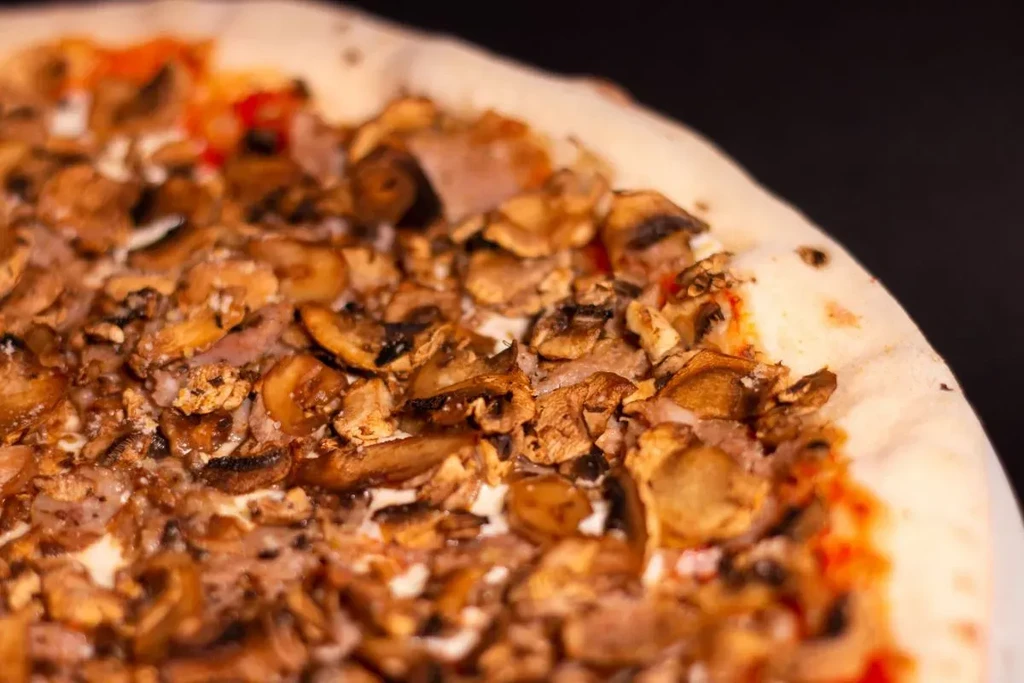 Close-up, top-down pizza with generous mushrooms, sliced meat, and two sauces.
