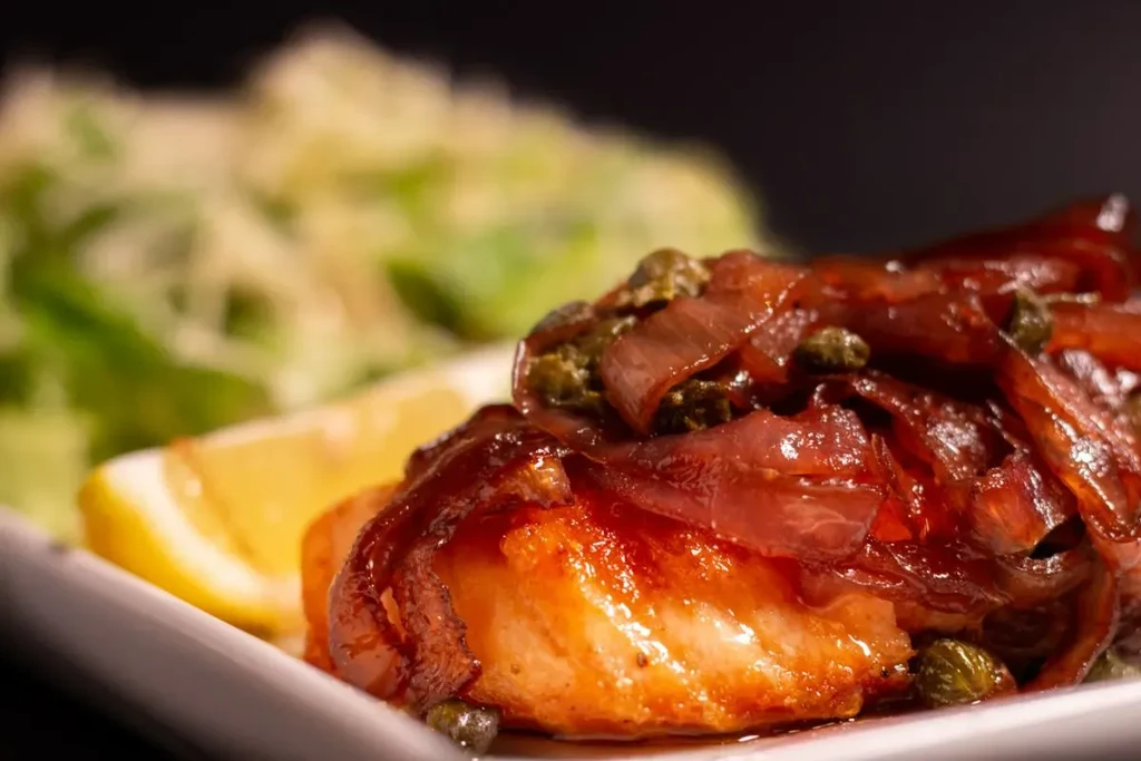Cooked fish with caramelized onions, capers, lemon, and blurred greens.