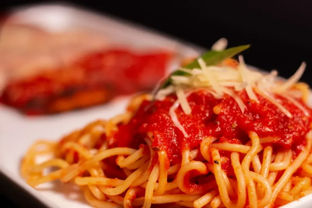 Close-up of spaghetti with red tomato sauce, cheese, and basil.