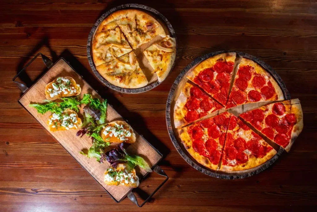Overhead: Two pizzas and bruschetta with creamy spread, cheese, herbs.