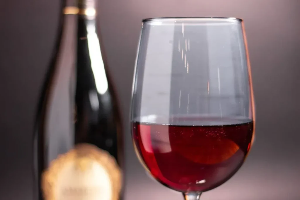 Glass of red wine, one-third full, blurred bottle behind.