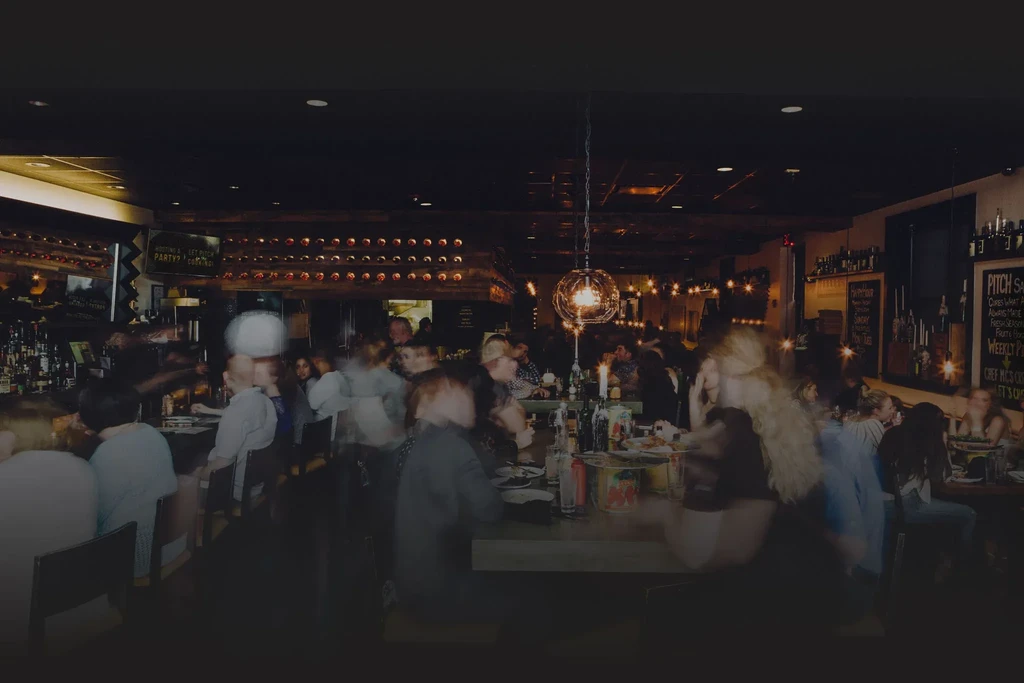 Bustling, dim restaurant interior with motion-blurred people and rustic wood.