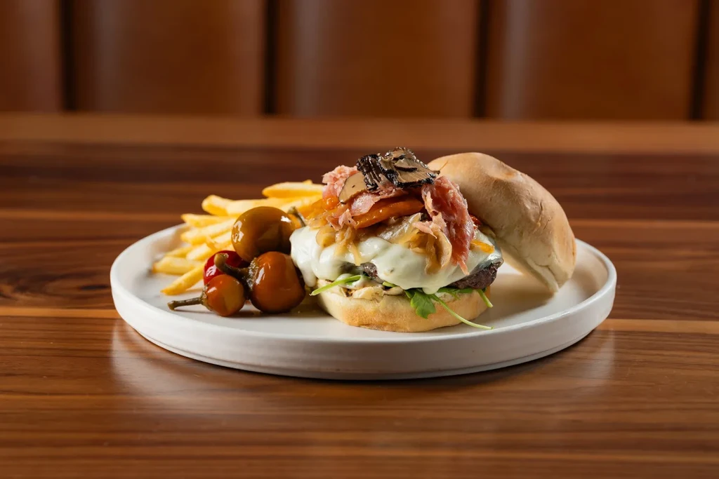 Gourmet burger with cheese, bacon, mushrooms, fries, and pickled peppers.