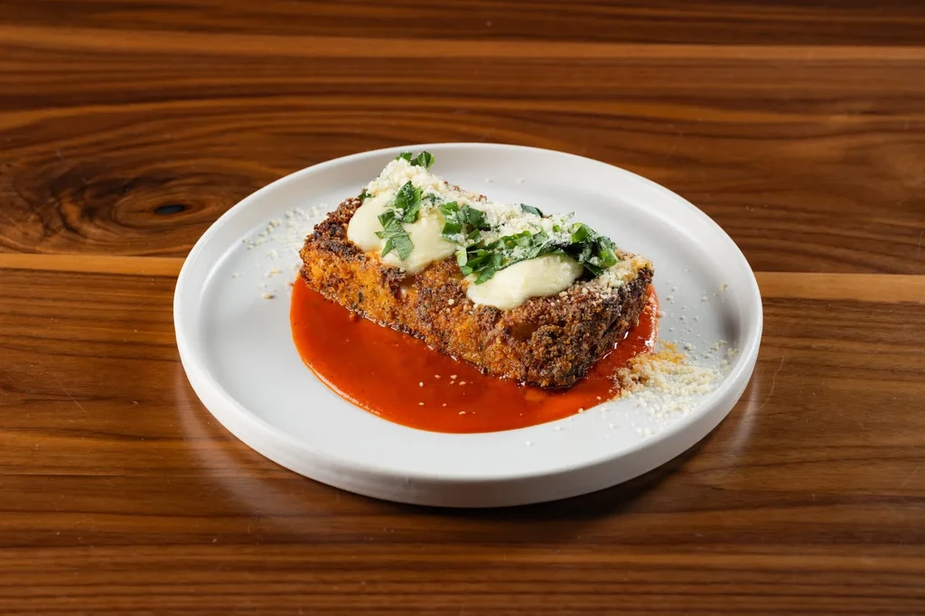 Golden-brown cutlet in red sauce with creamy dollops, herbs, and cheese.