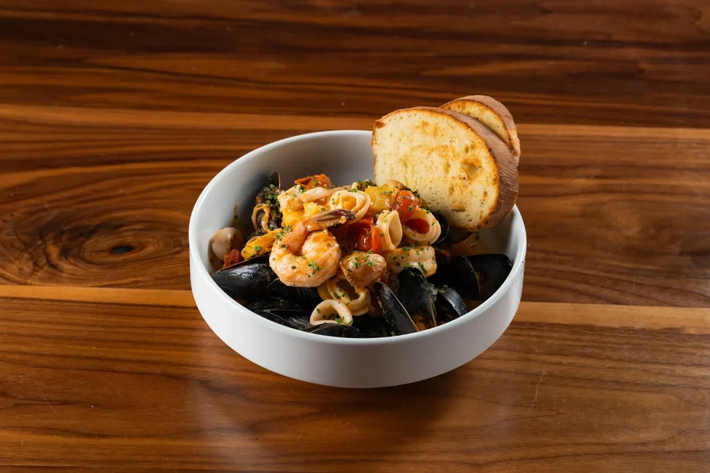 Vibrant seafood pasta bowl with mussels, shrimp, and garlic bread on wood.