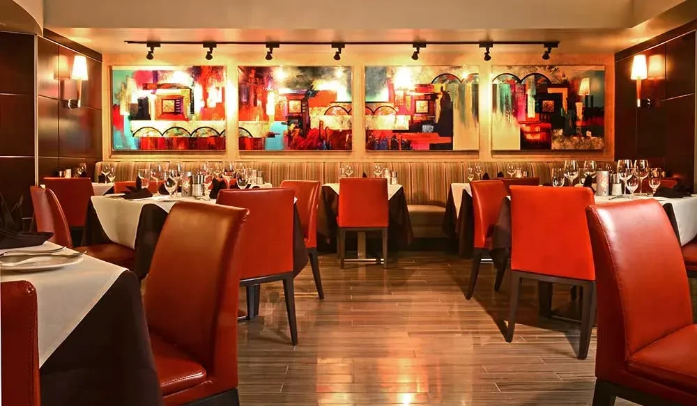 Modern restaurant dining room with set tables, terracotta chairs, and abstract art.