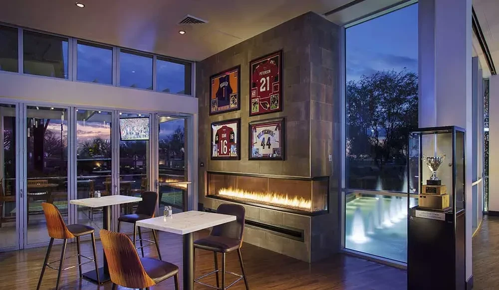 Upscale sports bar interior with fireplace, high-top tables, and outdoor view.