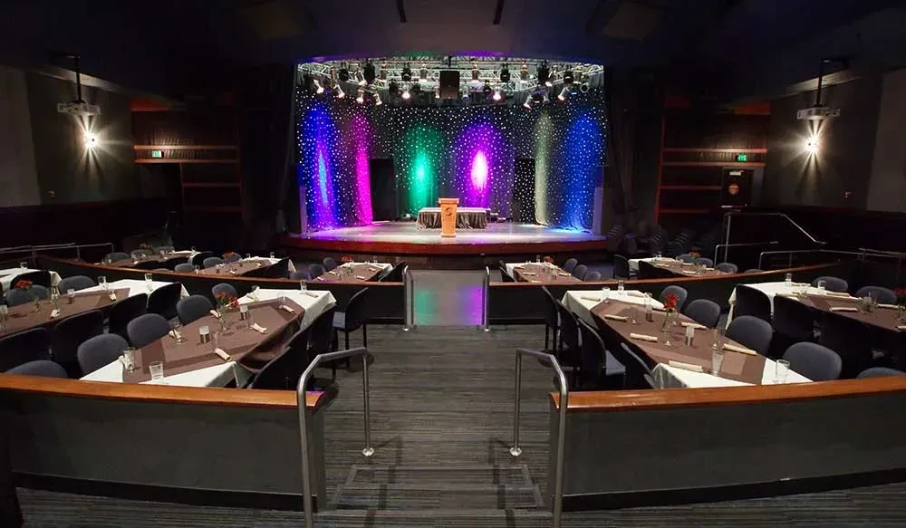 Colorful stage lights illuminate an empty dinner theater with set tables.
