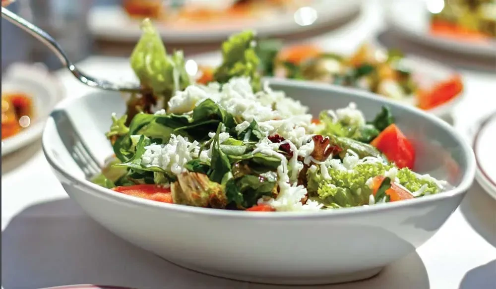 Close-up of fresh salad with lettuce, tomatoes, cheese, and a fork.