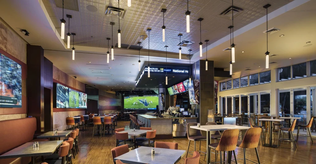 Modern sports bar with warm lighting, multiple TVs, and varied seating.