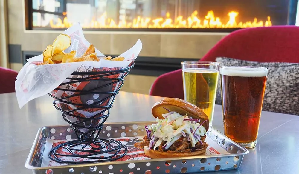 Pulled pork sandwich, chips, two beers, modern restaurant with fireplace.