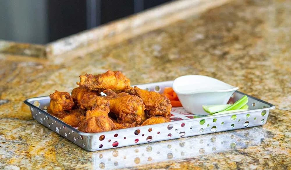 Golden-brown fried chicken wings in basket with ranch, celery, carrots.
