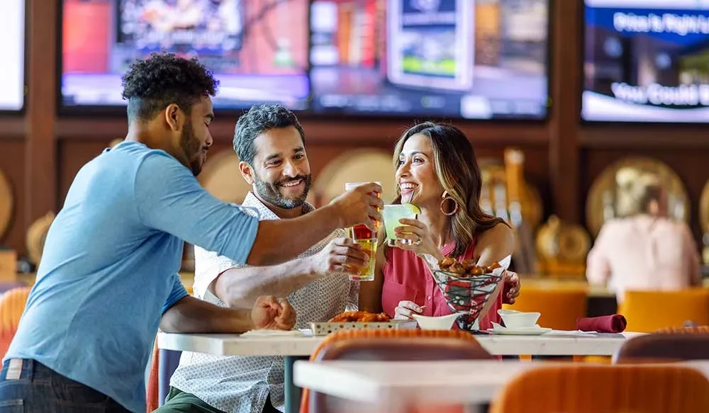 Friends clinking glasses with drinks and food at a sports bar.