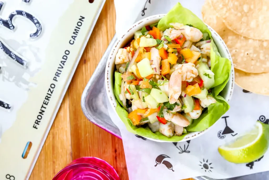 Overhead: Shrimp ceviche with chips and lime on a wooden surface.
