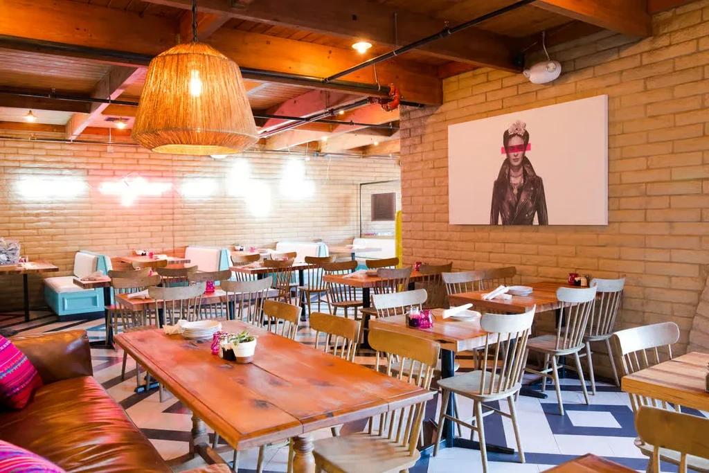 Empty restaurant interior with wooden tables, booth seating, brick walls, and geometric floor.
