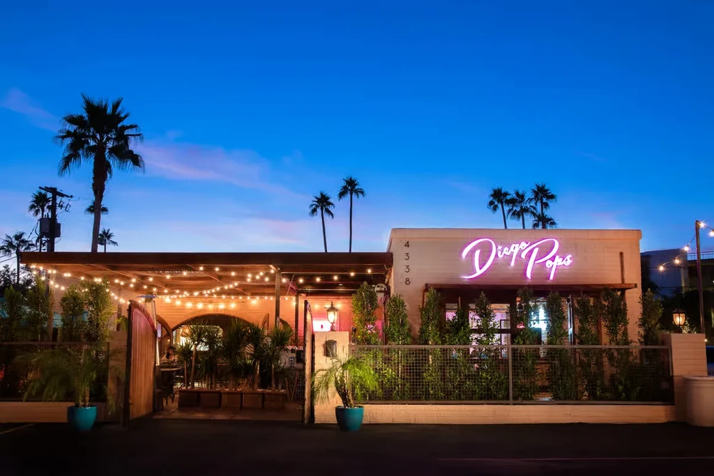 Diego Pops restaurant, pink neon sign, patio with lights under sunset sky.