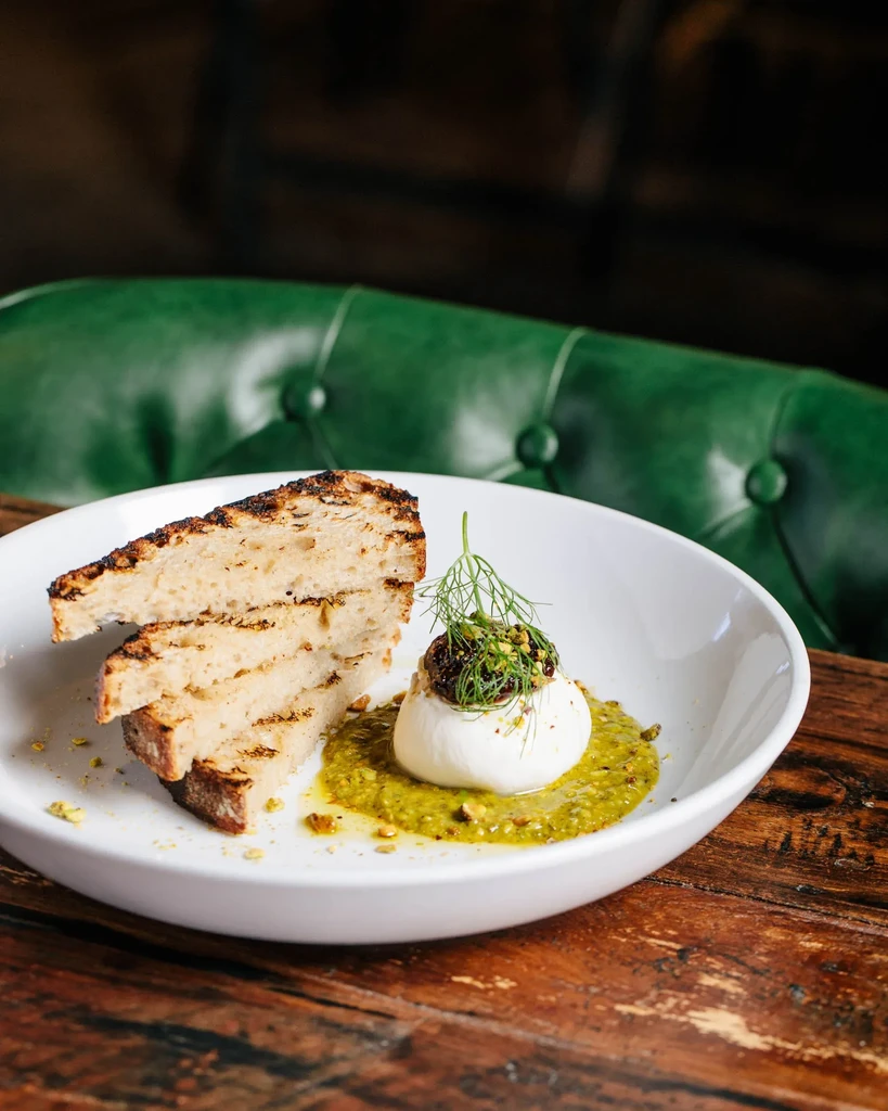 Plated burrata with green sauce, garnish, and grilled bread.