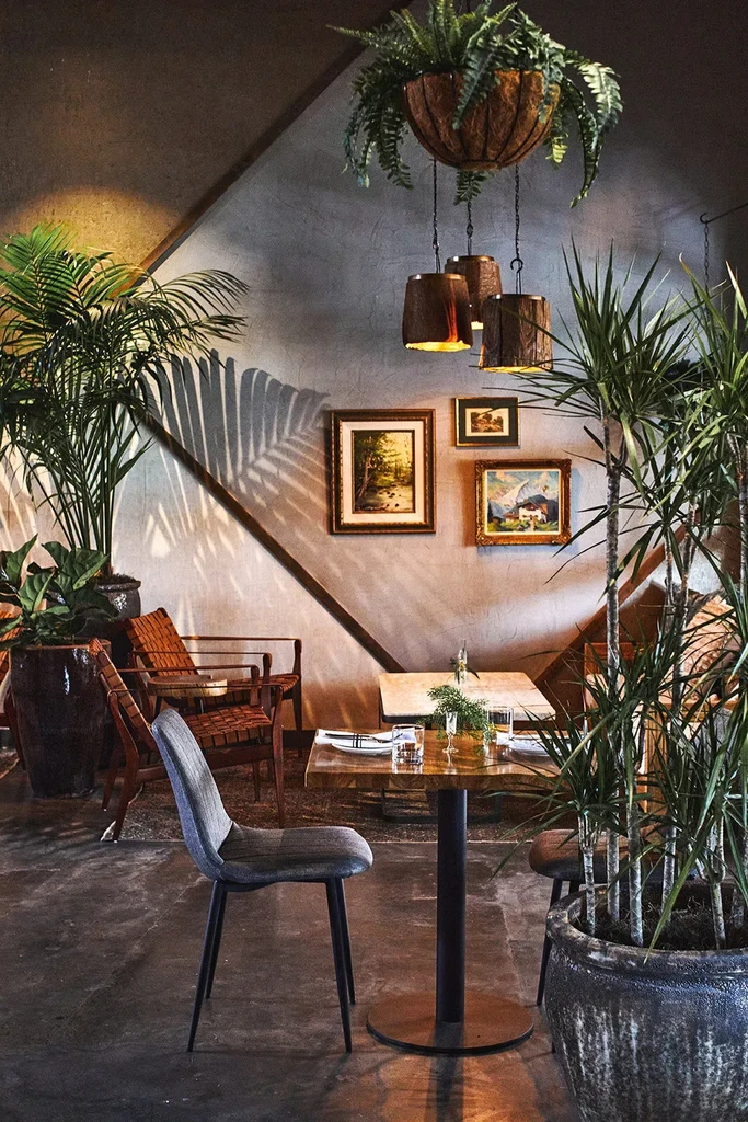 Cozy restaurant interior with lush plants, wood lights, and concrete walls.