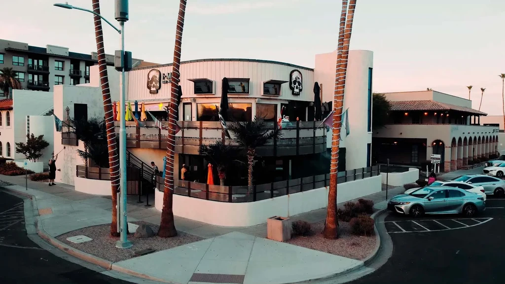 Modern multi-level building with skull logos, colorful umbrellas, and palm trees.